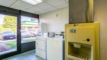 A laundromat with dryers, a coin-operated ice dispenser, and a view of parked cars outside.
