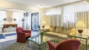 A hotel room with a sofa, armchairs, a glass coffee table, a side table with a lamp, a mirror, and a view of the outside through a door. - Americas Best Value Inn Edgewood (Edgewood)
