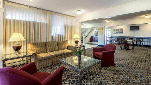 A hotel lobby with a sofa, armchairs, a glass coffee table, and a dining area with chairs and tables. - Americas Best Value Inn Edgewood (Edgewood)
