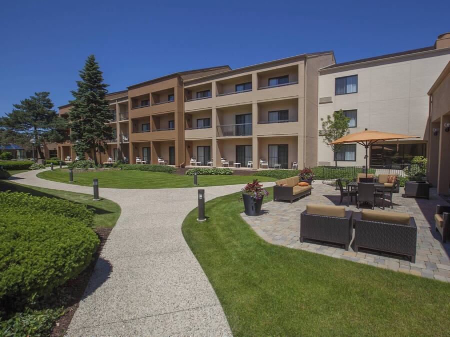 A courtyard with a paved walkway, outdoor seating area with wicker furniture, and a building with multiple balconies.