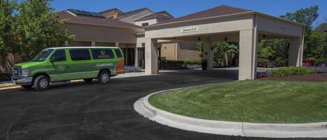A green van parked in front of a building with a covered parking area and a clear sky.