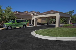 A green van parked in front of a building with a covered parking area and a clear sky.