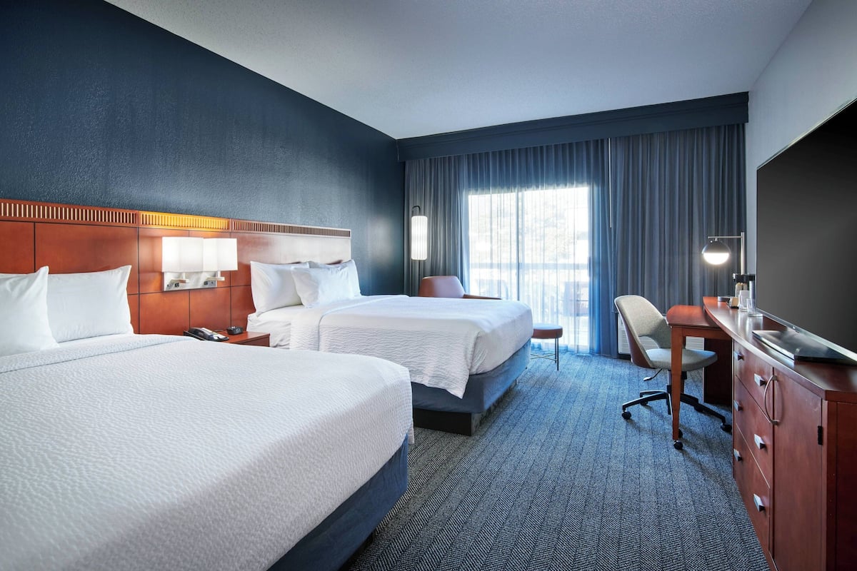 A hotel room with two beds, a desk, a chair, and a TV.