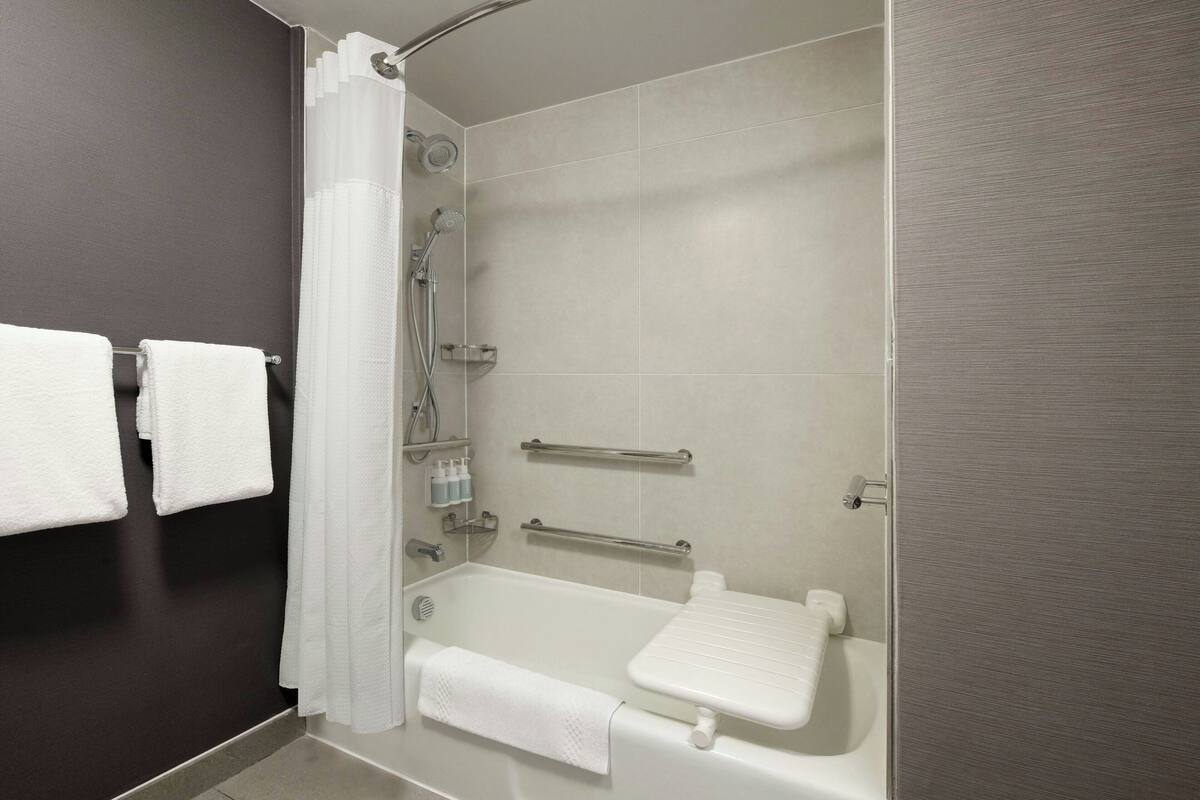 A modern bathroom with a bathtub, shower, and handrails.