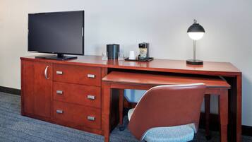 Un espacio de trabajo en un hotel con un escritorio de madera, un televisor, una cafetera y una silla.
