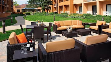An outdoor seating area with wicker furniture, a table with wine bottles, and a path leading to a building.