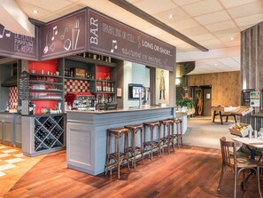 Een bar met een toonbank, krukken en planken vol flessen en glazen.