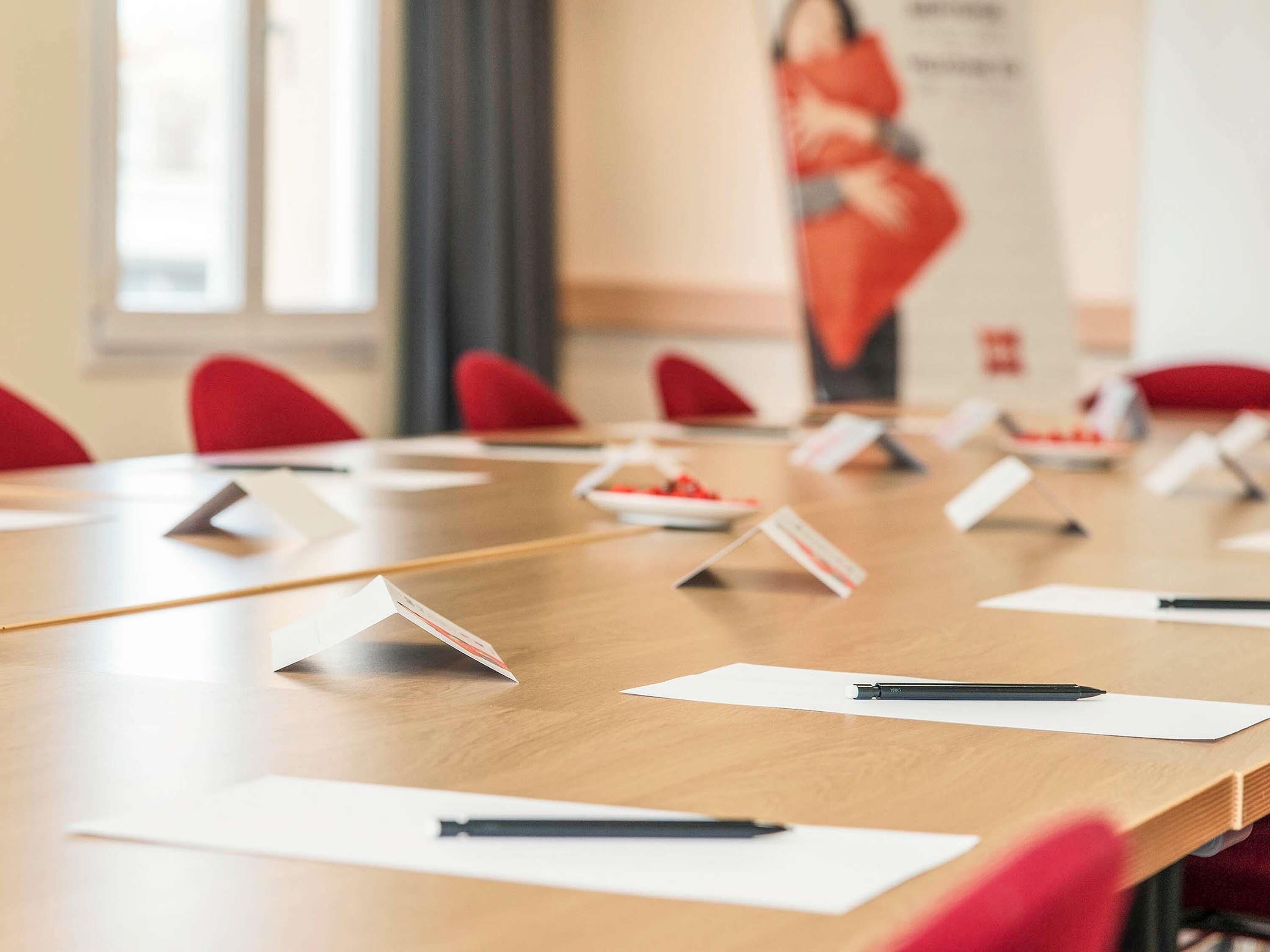 A conference room with a long table, red chairs, nameplates, and pens on the table.