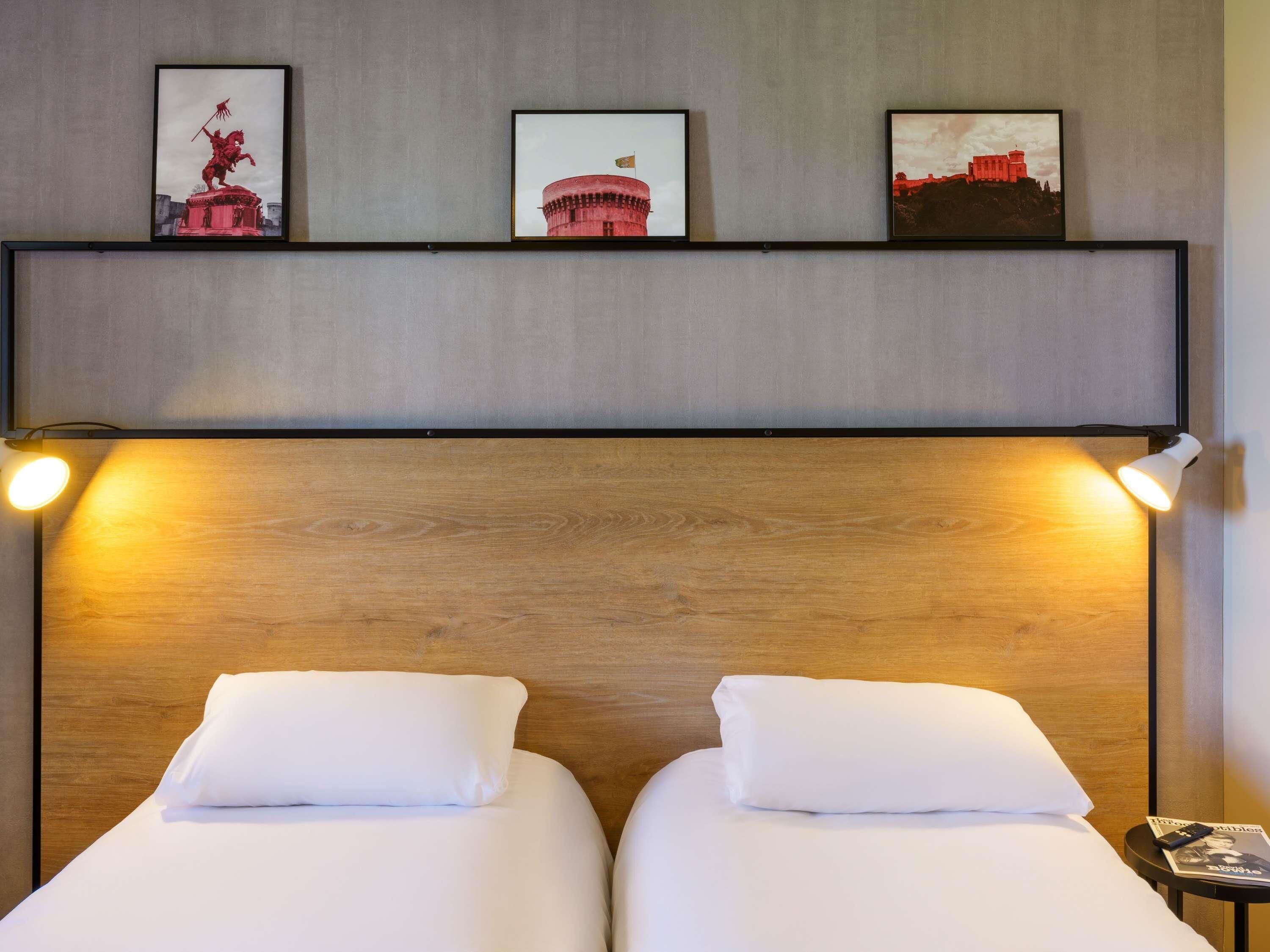 A hotel room with two beds, a wooden headboard, and three framed pictures on the wall.