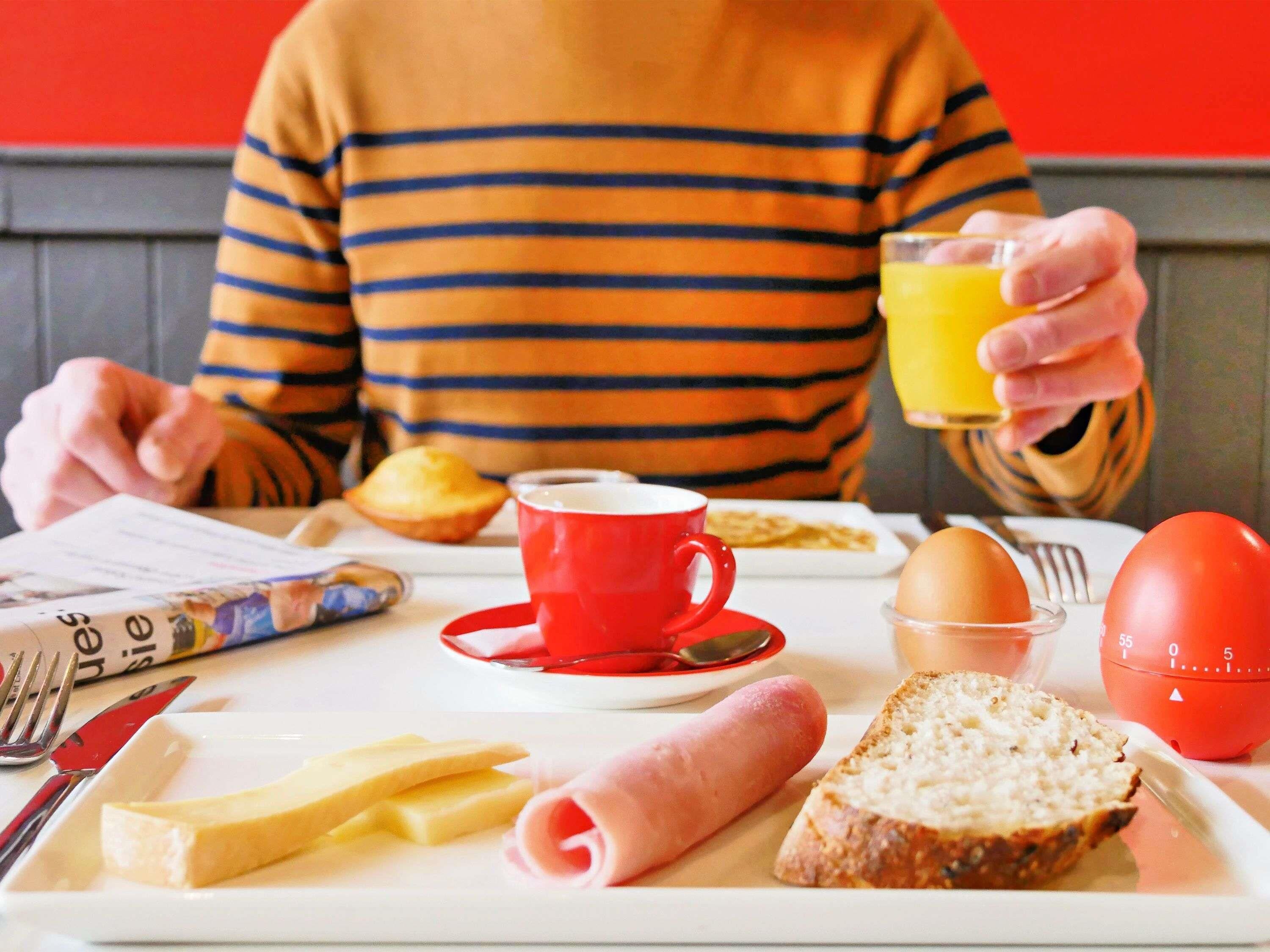 Un plateau de petit-déjeuner avec des œufs, des toasts, du jambon, du fromage et une tasse rouge.