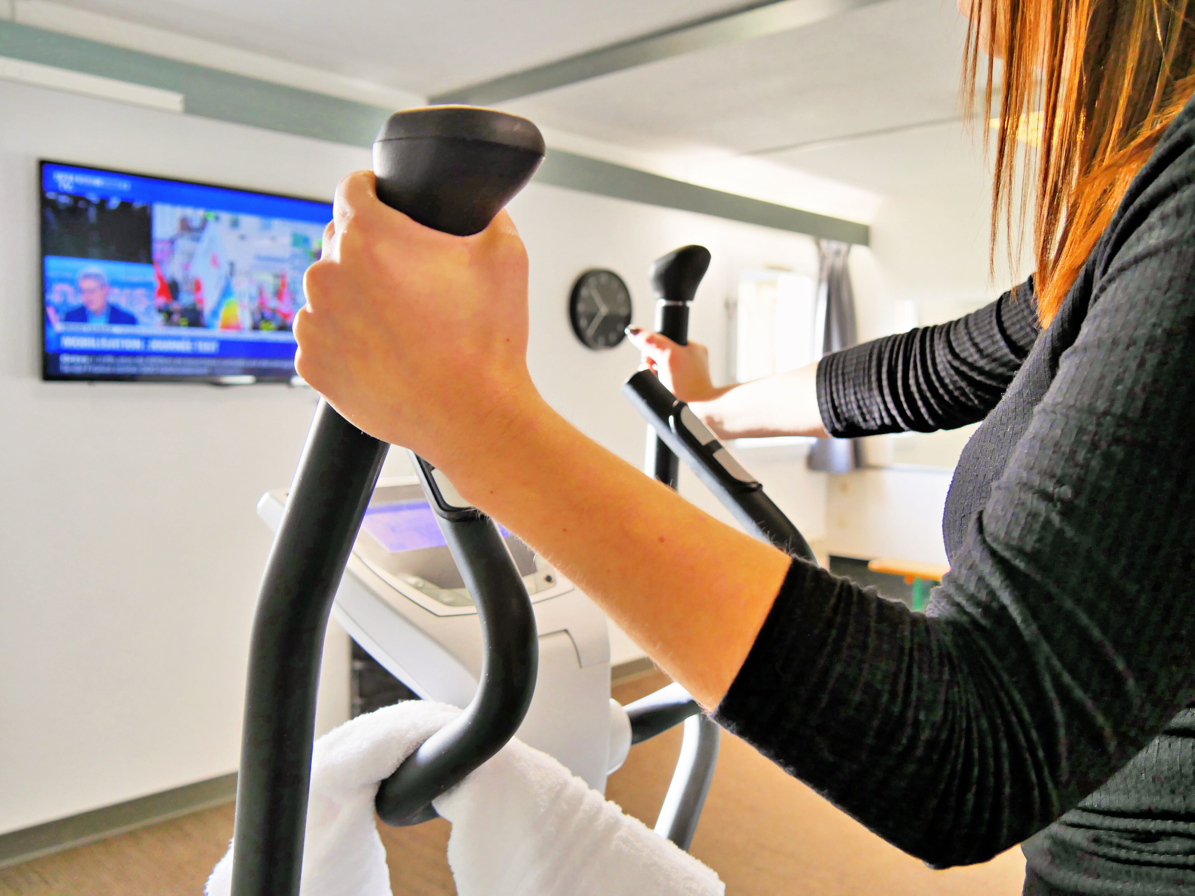 Una persona usando una bicicleta estática en una habitación donde un televisor muestra un evento deportivo.