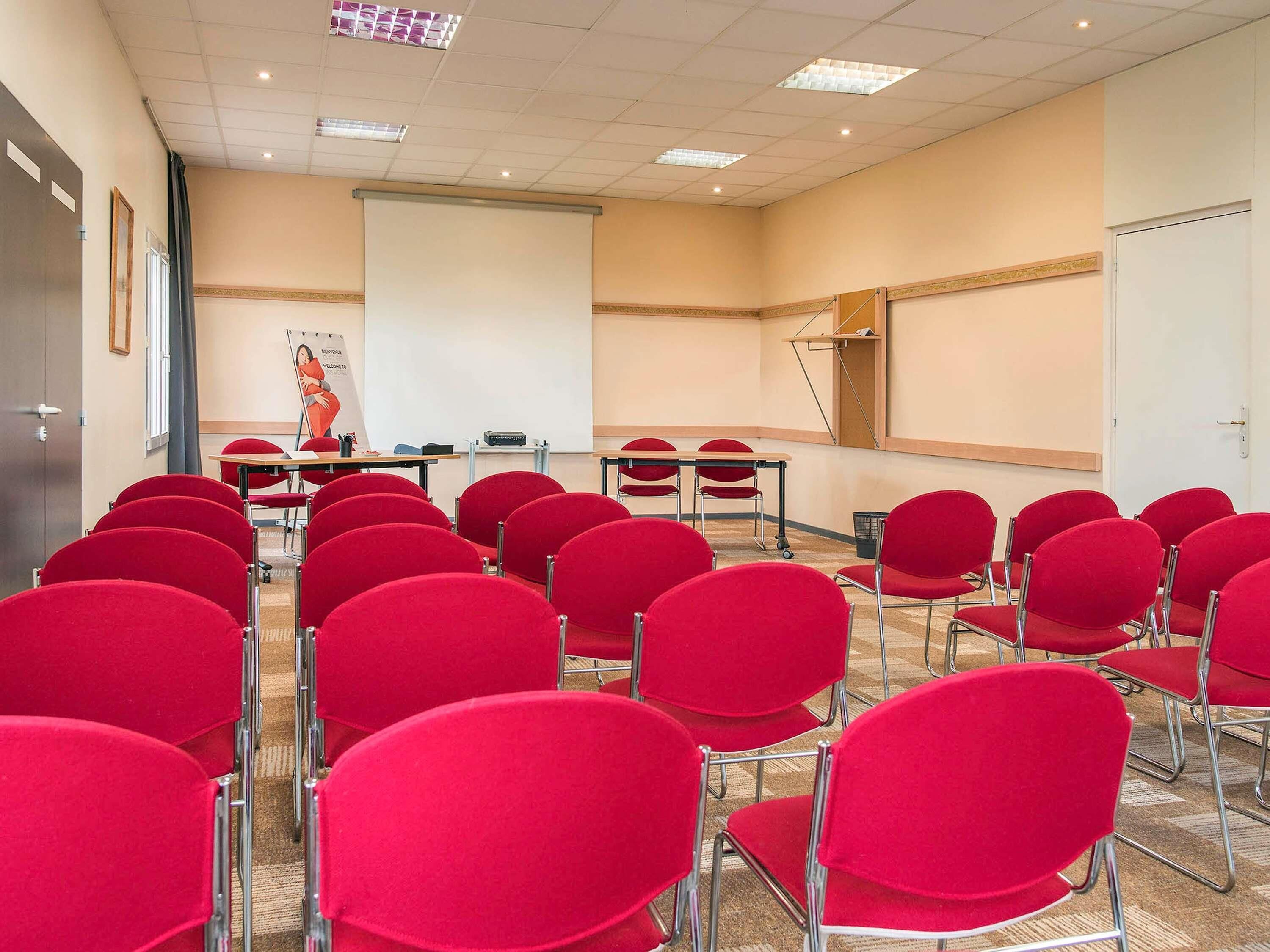 A conference room with red chairs, a projector screen, and a presentation area.