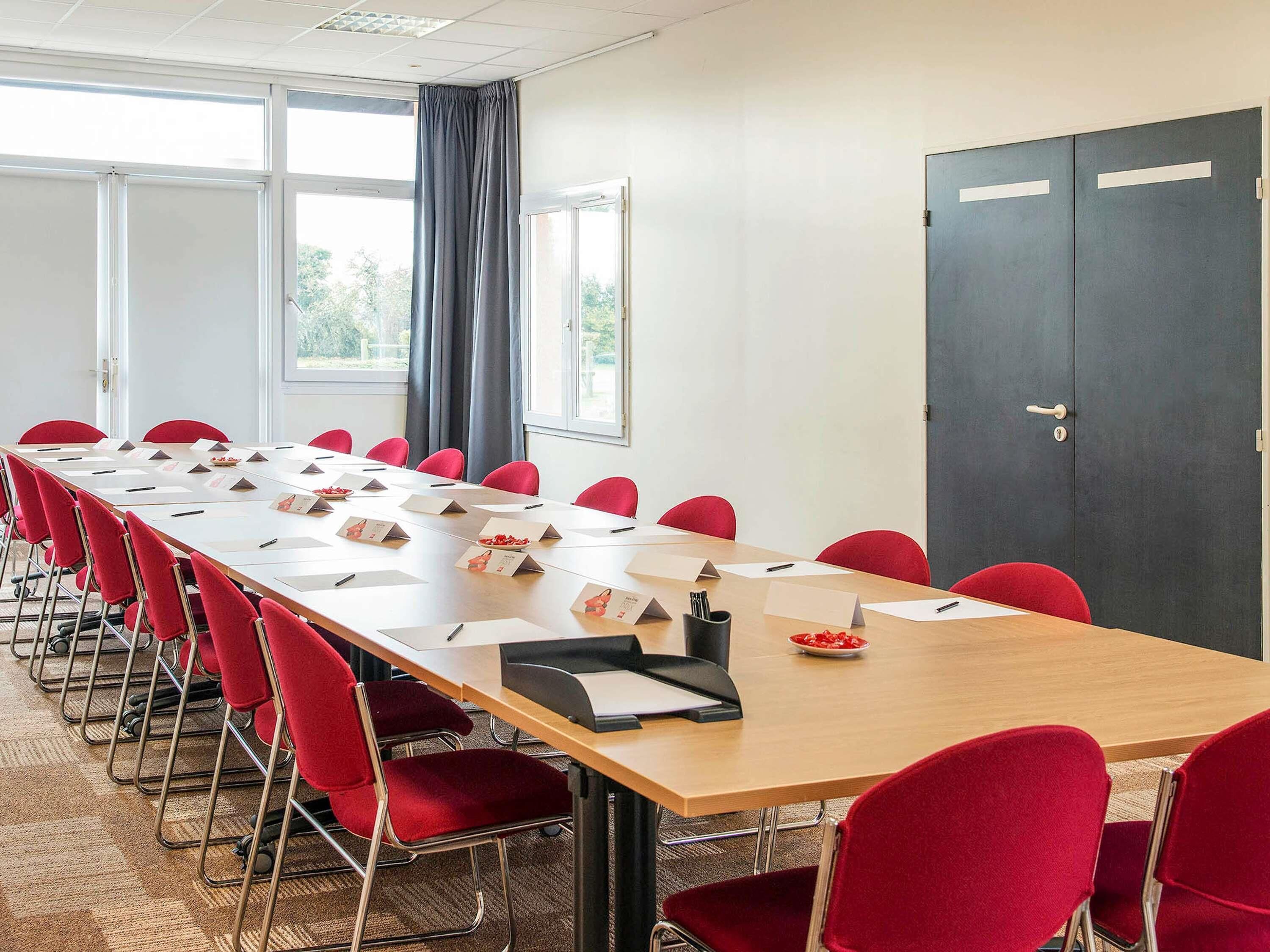 A conference room with a long table, red chairs, name cards, and a dark door.