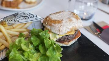 Un repas composé d’un hamburger, de frites et de laitue, servi sur une assiette en ardoise noire.