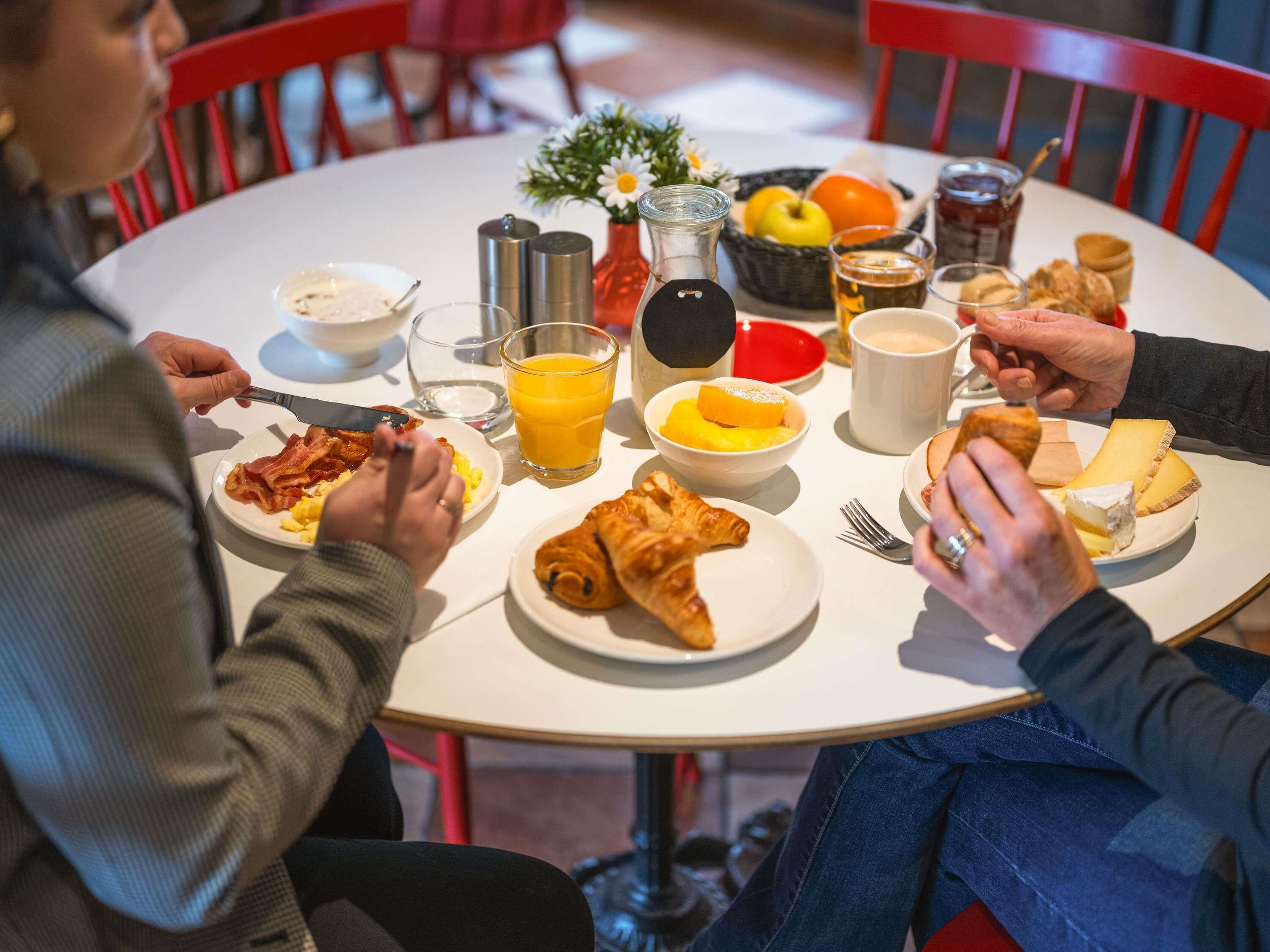 Una mesa redonda para comer con alimentos para el desayuno, incluyendo huevos, tocino, queso y bollería.