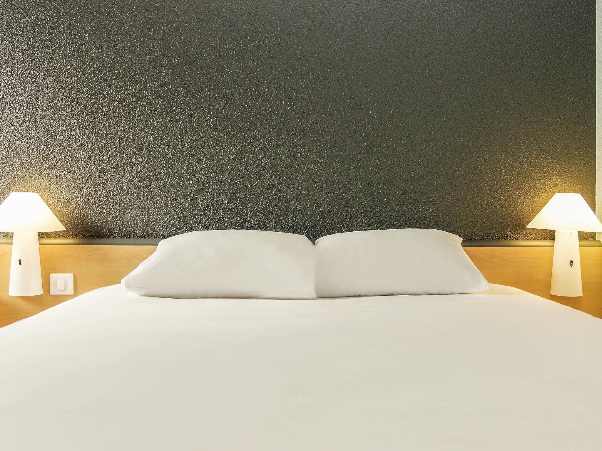 A hotel room with a large bed, two bedside lamps, and a textured wall.