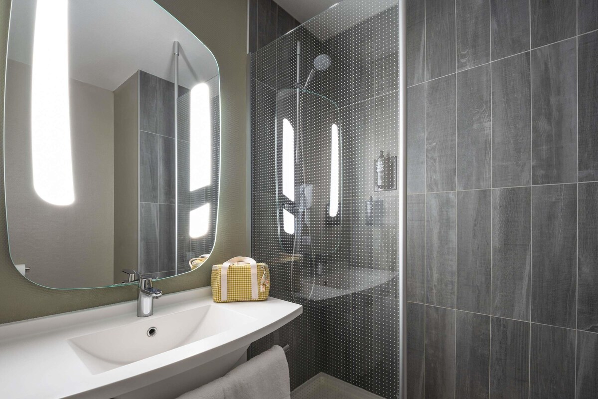 Une salle de bain moderne avec un grand miroir, un lavabo et un espace douche.