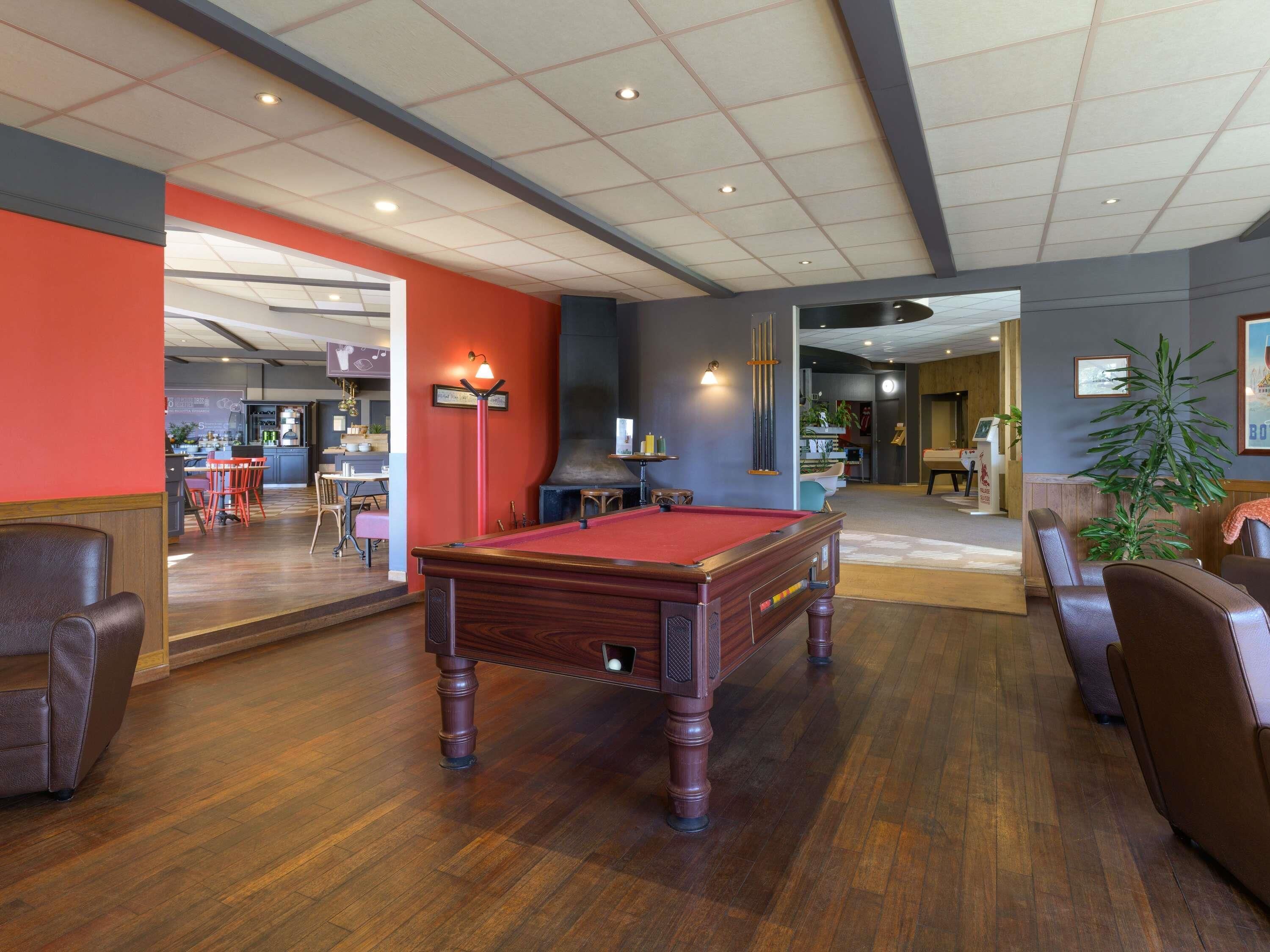 A billiards table in a room with a wooden floor, a bar area, and seating.