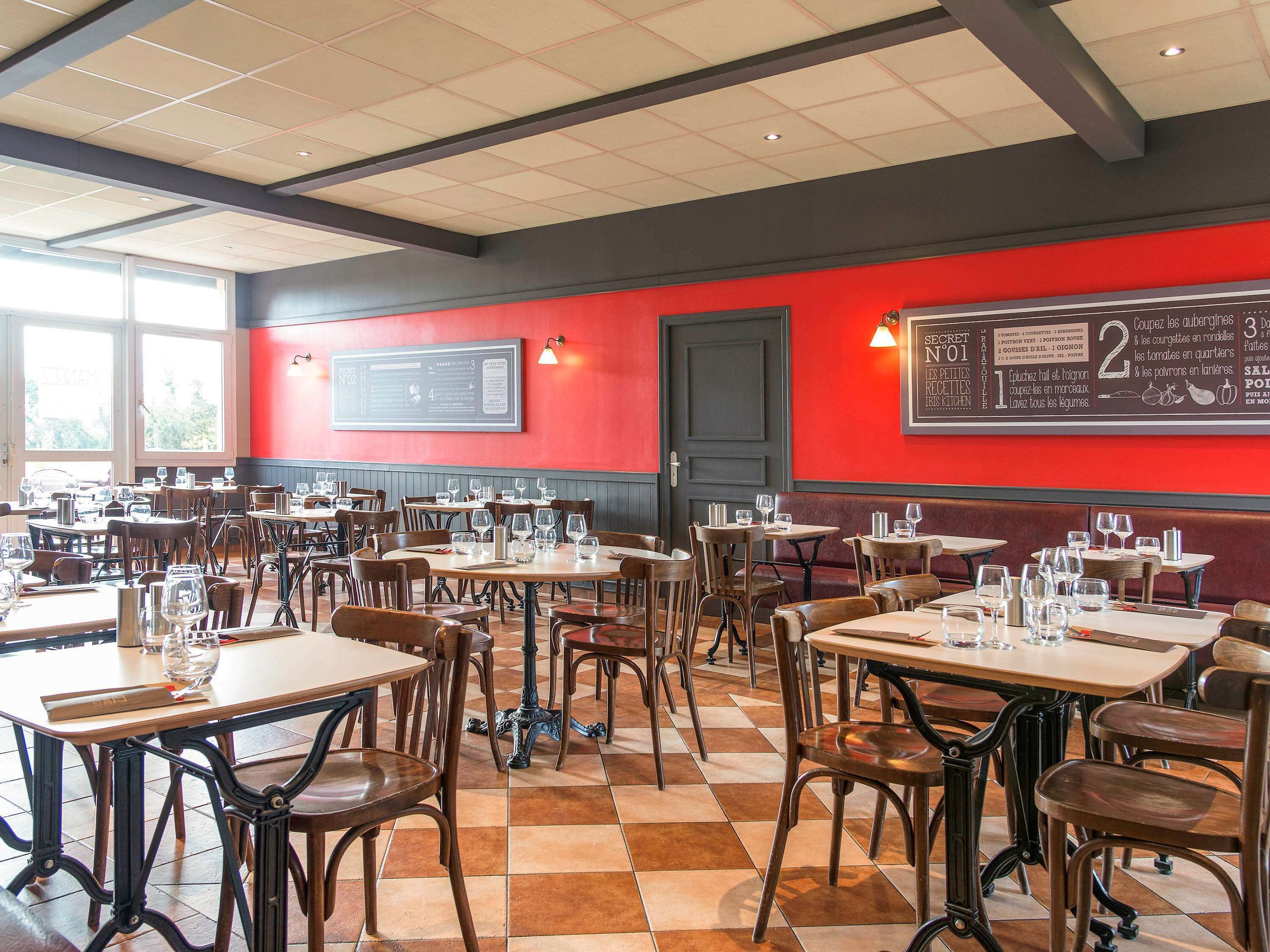 L’intérieur d’un restaurant, avec plusieurs tables et chaises, un mur d’accent rouge et un panneau affichant le menu.