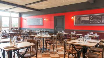 L’intérieur d’un restaurant, avec plusieurs tables et chaises, un mur d’accent rouge et un panneau affichant le menu.