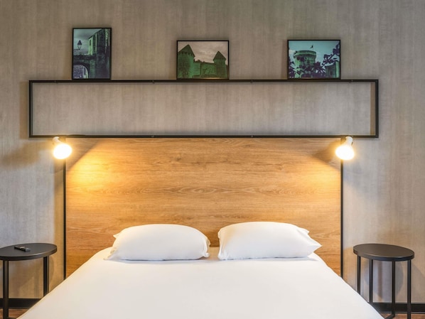 A hotel room with a wooden headboard, two bedside tables, a bed with white bedding, and three framed pictures on the wall.
