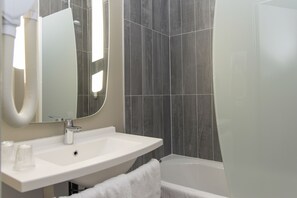 A modern bathroom with a white sink, mirror, and bathtub.