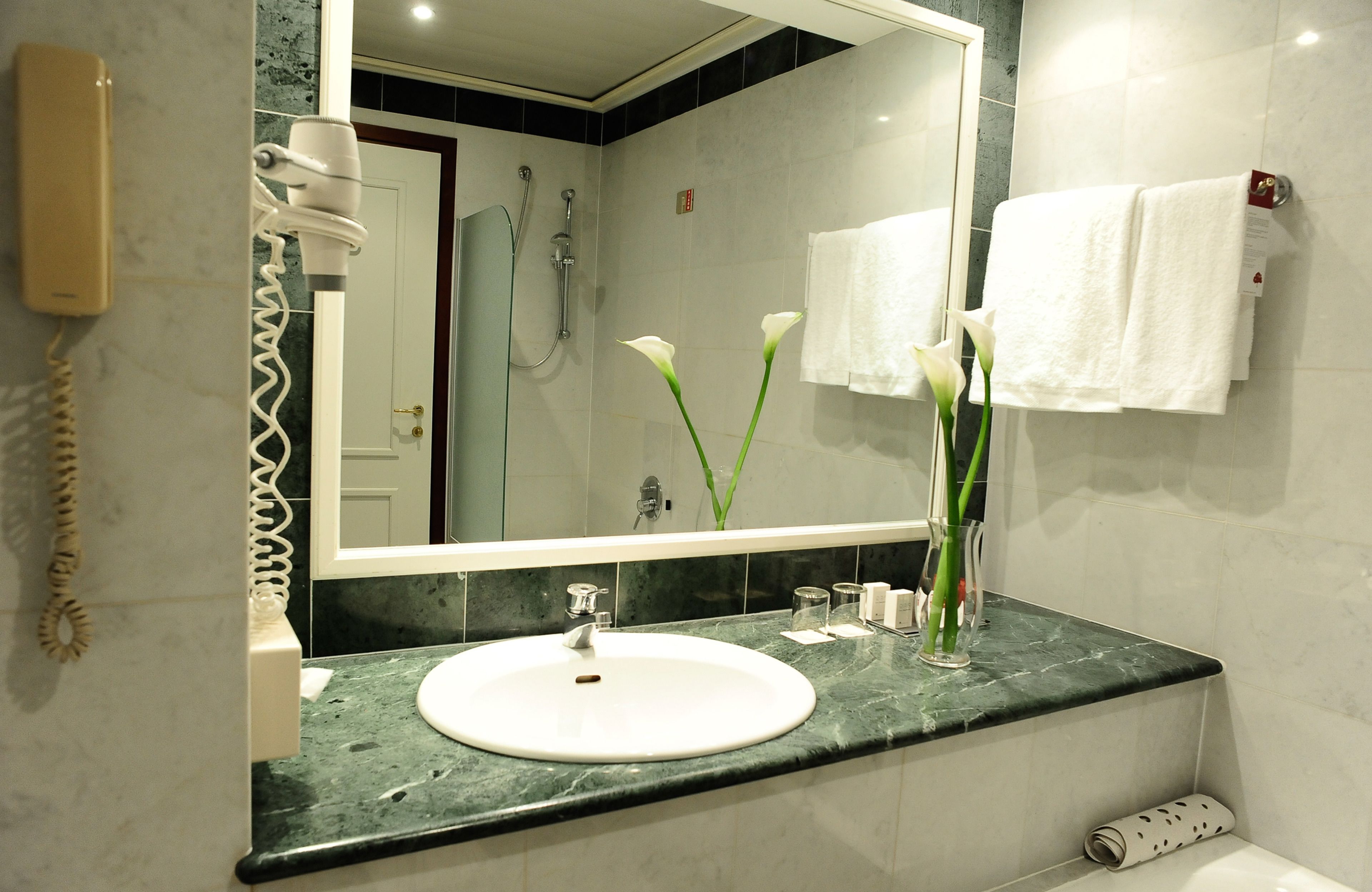 Une salle de bain avec un grand miroir, un lavabo, un sèche-cheveux et un porte-serviettes.