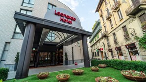 El exterior del Hotel Leonardo, con una entrada moderna, un césped bien cuidado y arquitectura europea tradicional.