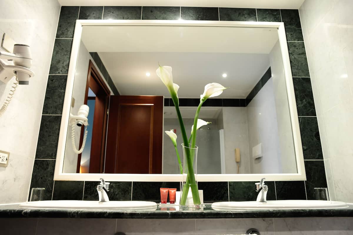 Un baño con un espejo grande, dos lavamanos, un secador de pelo y un florero con flores.