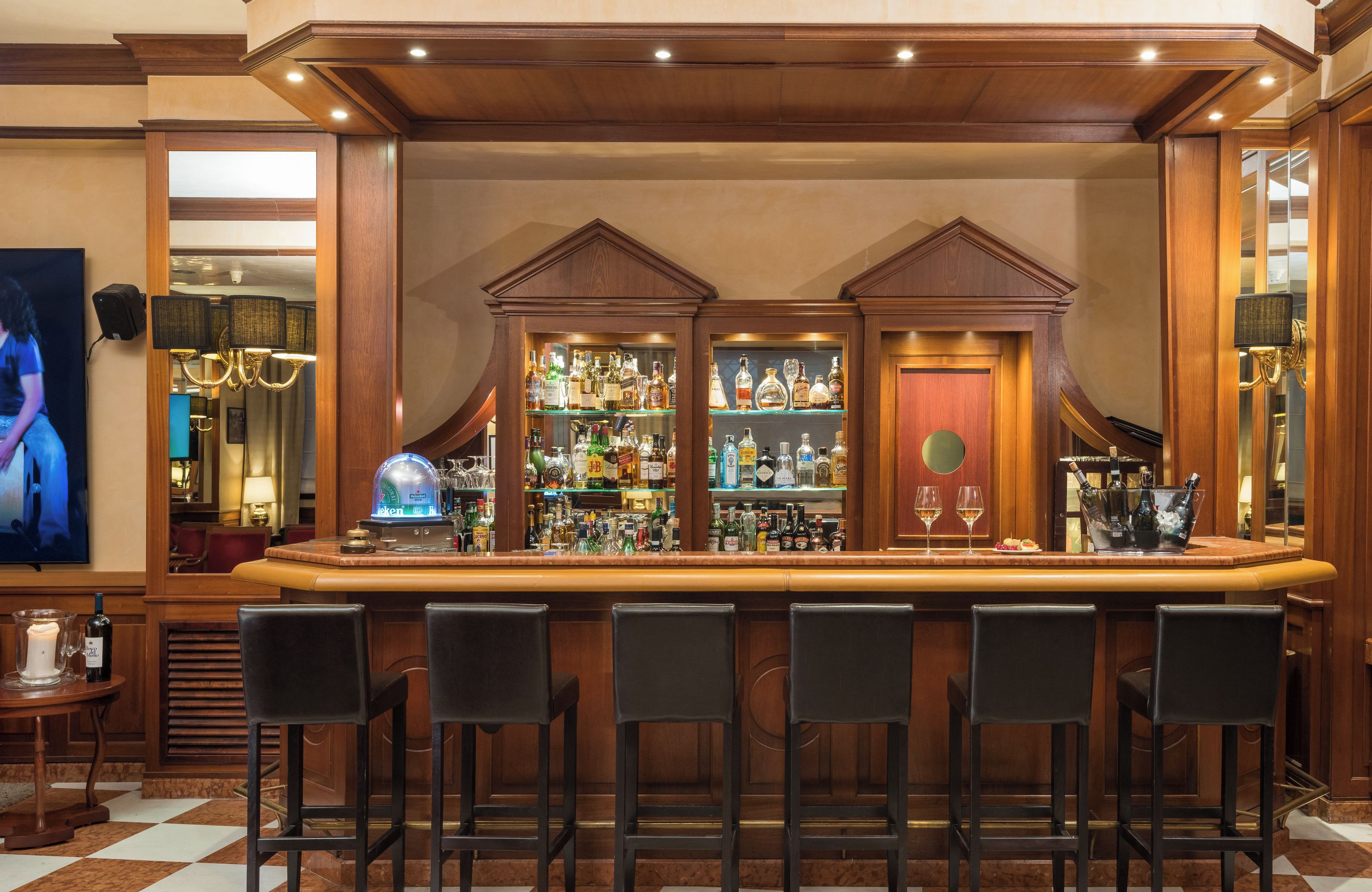 A bar area with a wooden bar counter, multiple shelves of liquor bottles, and several black bar stools.