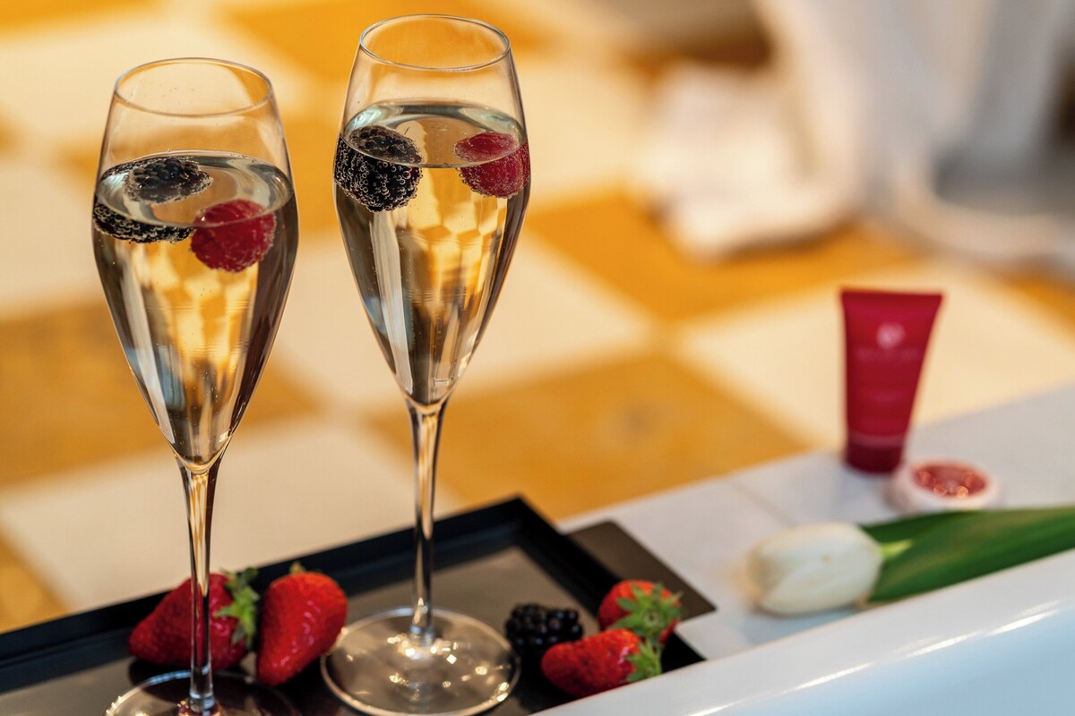 Dos copas de champán con frutos rojos sobre una bandeja, fresas, una tulipa y un tubo rojo sobre una mesa a cuadros.