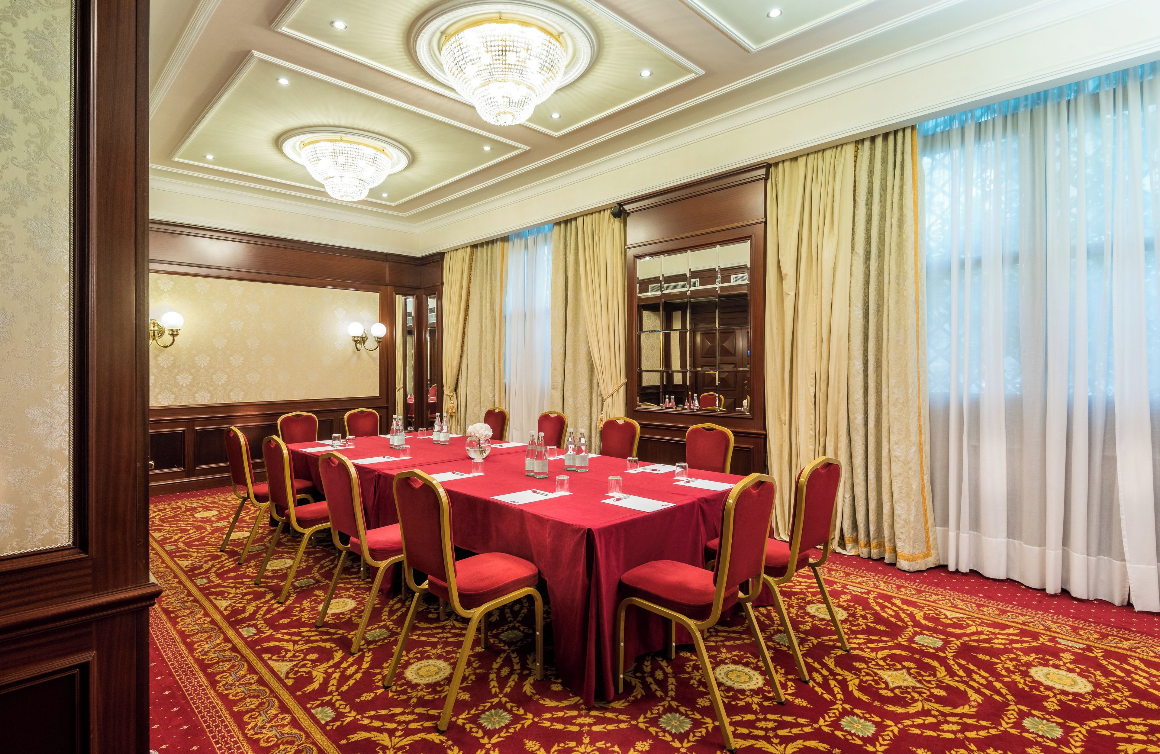 Uma sala de conferências com carpete vermelho, mesas redondas e cadeiras vermelhas.