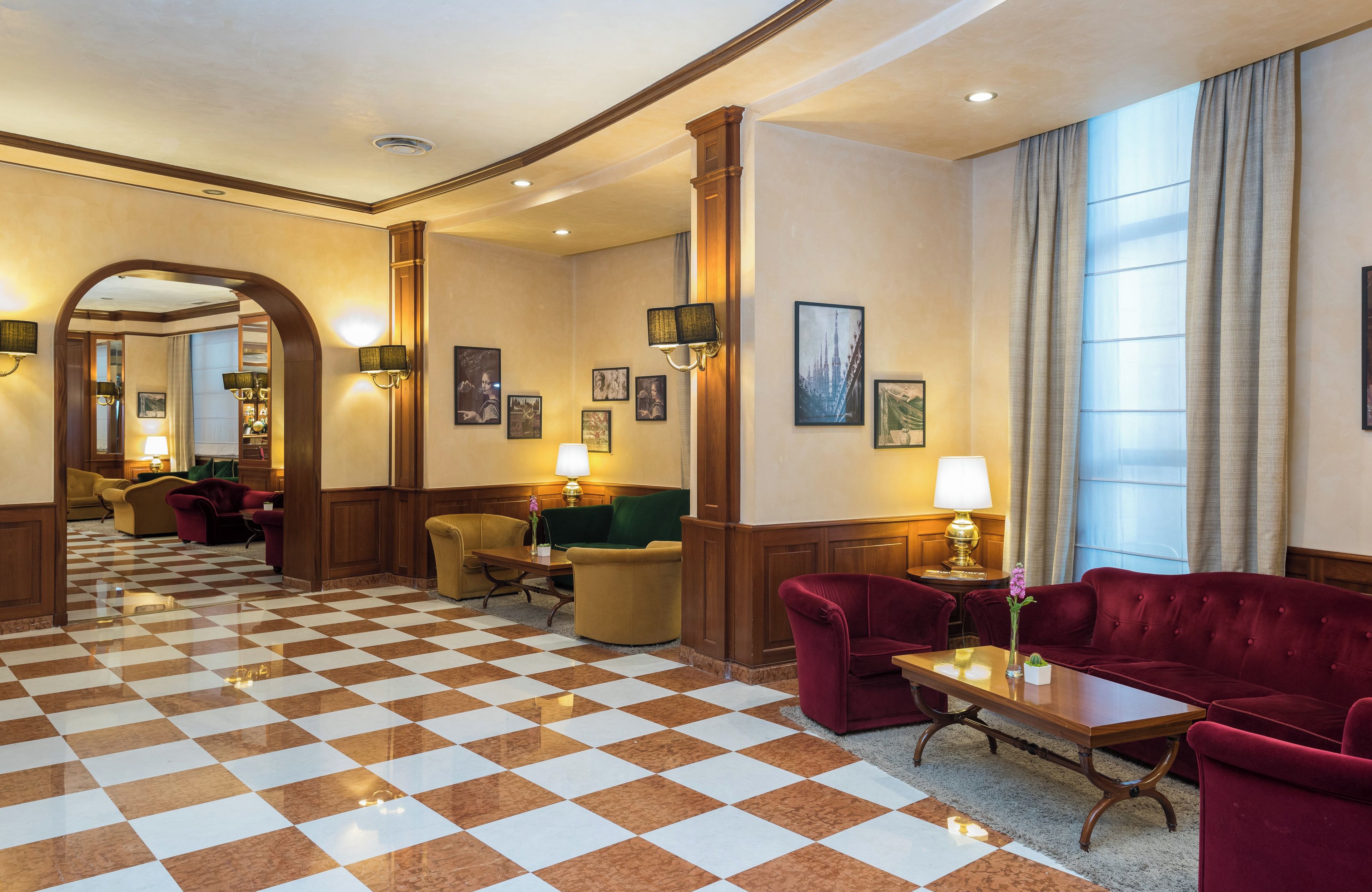 Eine Hotelhalle mit Schachbrettboden, mehreren Sitzbereichen und gerahmten Kunstwerken an den Wänden.
