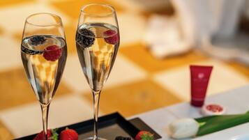 Two champagne flutes with fruit garnishes on a tray, accompanied by strawberries and a red tube, likely a cosmetic product, on a checkered tablecloth.