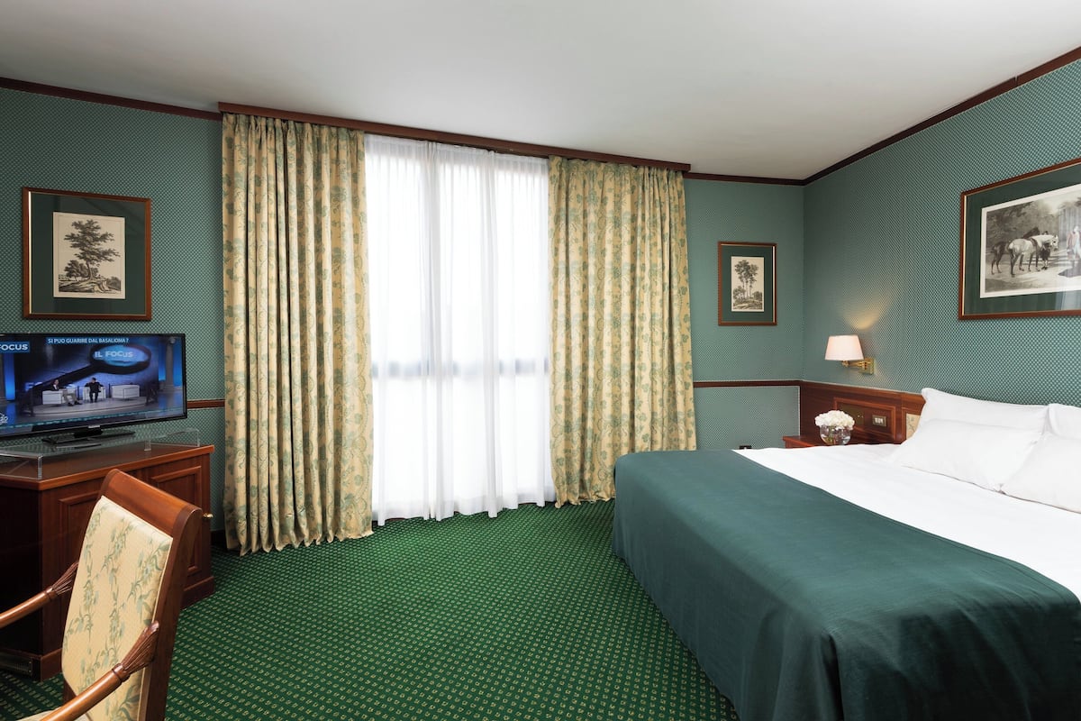 Une chambre d’hôtel avec un lit, un bureau avec une télévision, une chaise et des rideaux.