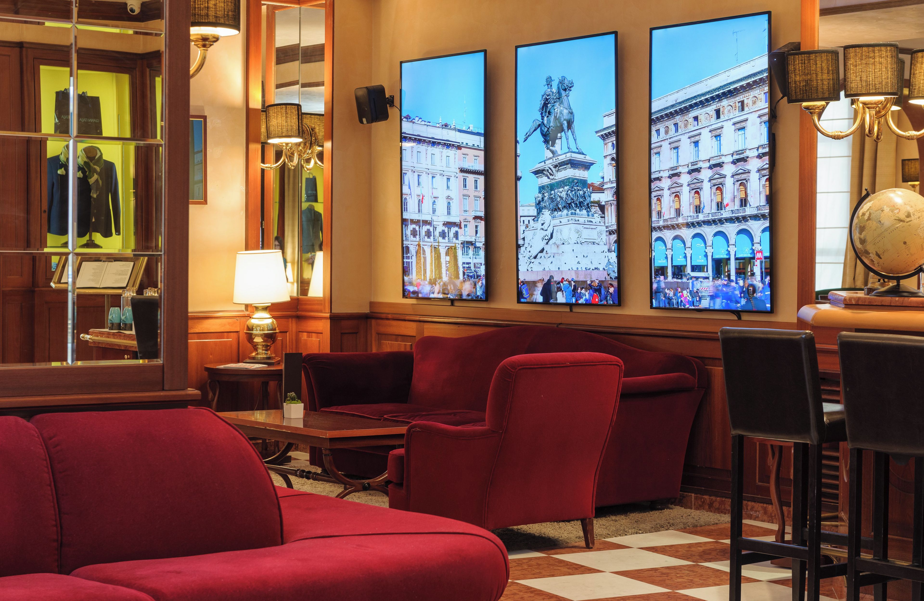A hotel lobby with red sofas, a checkered floor, and three large wall-mounted screens displaying cityscapes.