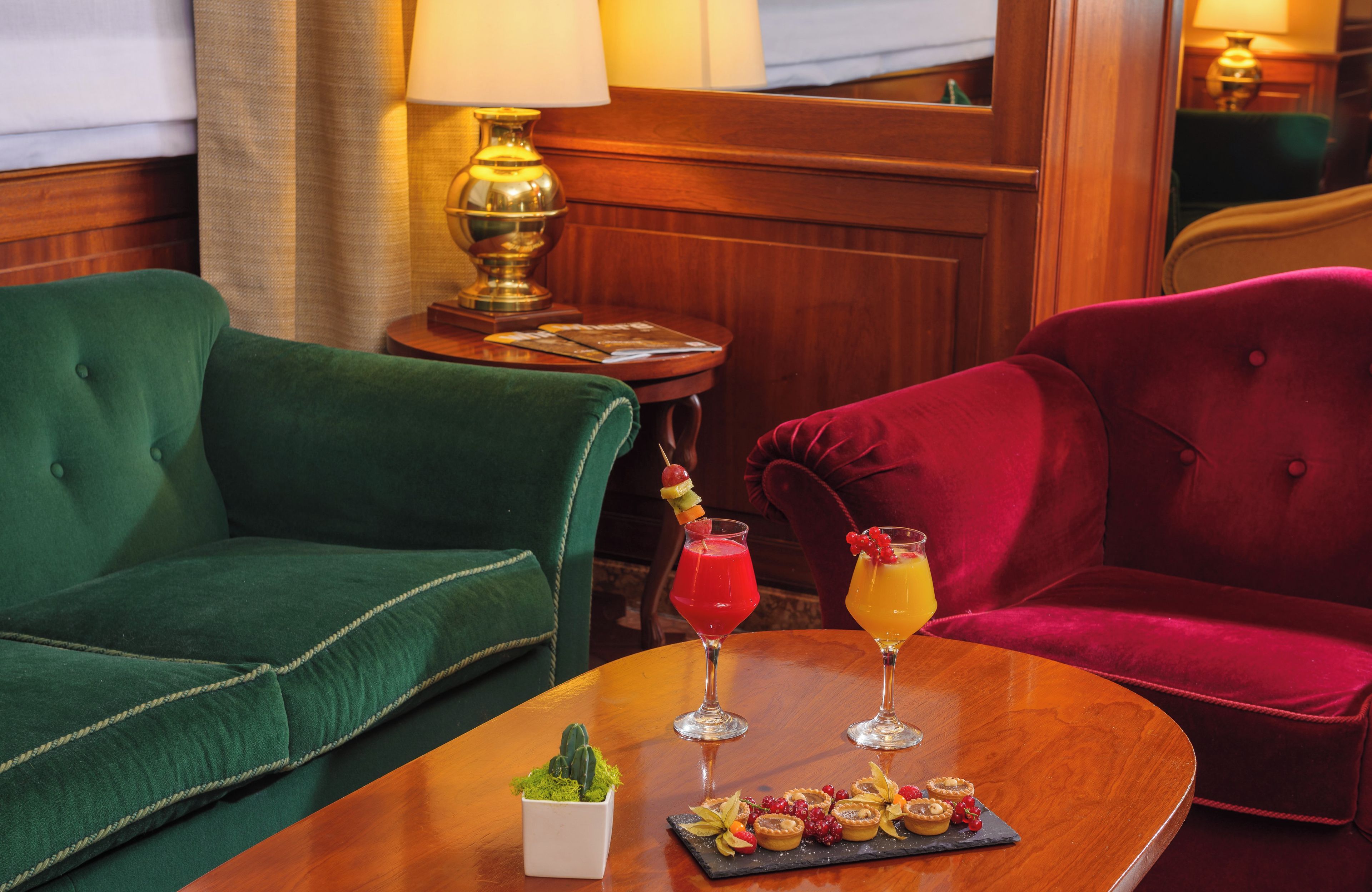 A room with a green sofa, a red sofa, and a wooden table with two drinks and a dessert tray.