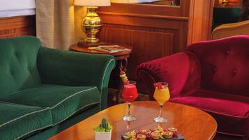 A room with a green sofa, a red sofa, and a wooden table with two drinks and a dessert tray.