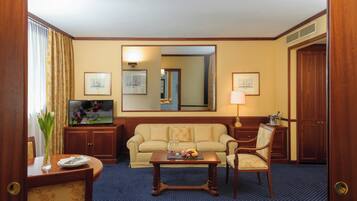 A hotel room with a sofa, armchairs, a coffee table, a TV, a mirror, and framed pictures on the wall.
