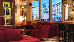 Un vestíbulo de hotel con sofás rojos, piso a cuadros y tres pantallas grandes murales mostrando paisajes urbanos.