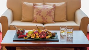 Una mesa con una bandeja de frutas y dos vasos de agua, sobre una mesa de madera frente a un sofá beige con un cojín estampado.