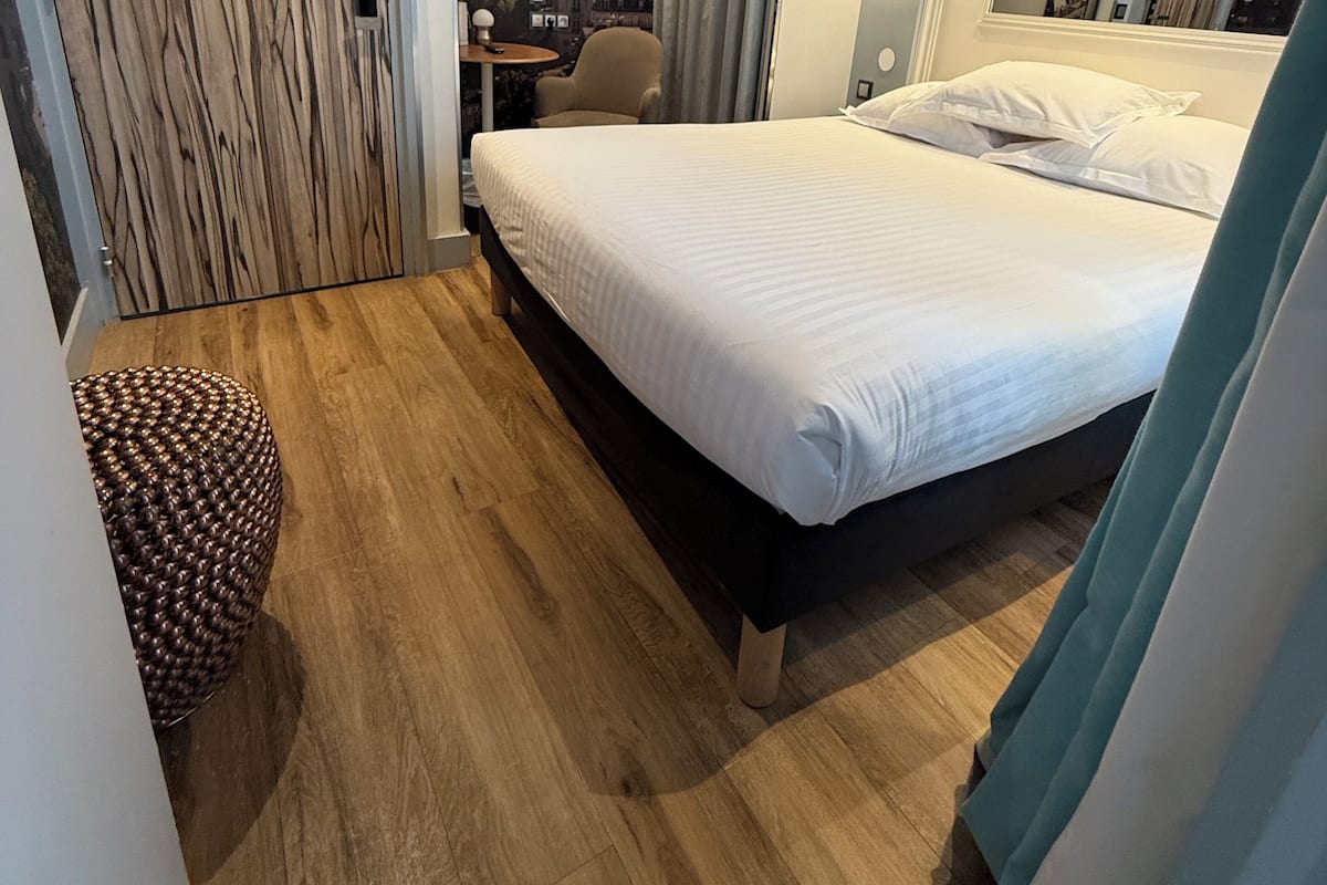 A hotel room with a bed, a desk, a chair, a wooden floor, and a cityscape mural on the wall.