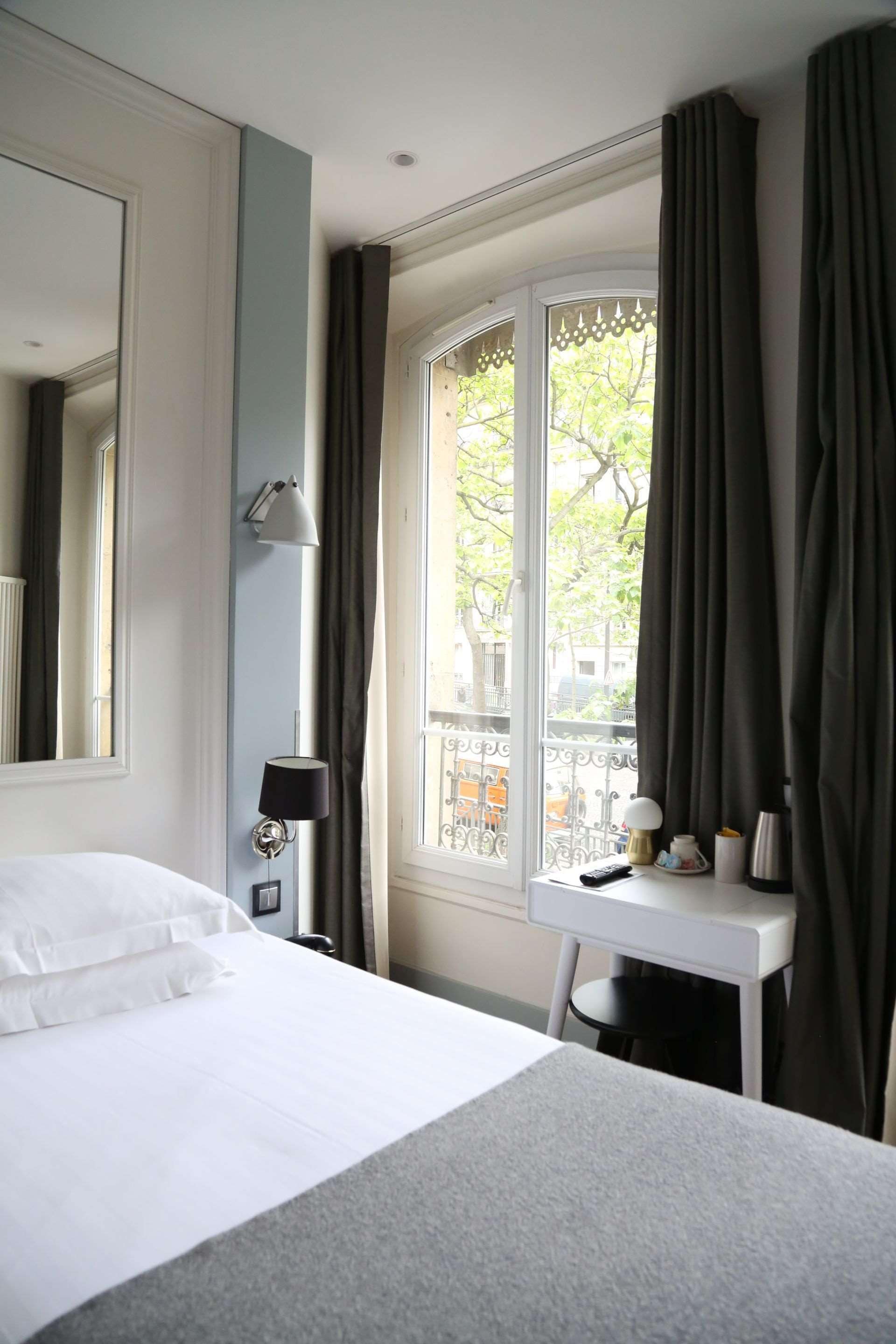 Une chambre d’hôtel avec un lit, un bureau, une lampe et une fenêtre avec des rideaux.