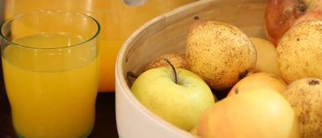 A pitcher of orange juice, a glass of orange juice, and a bowl of apples on a table.