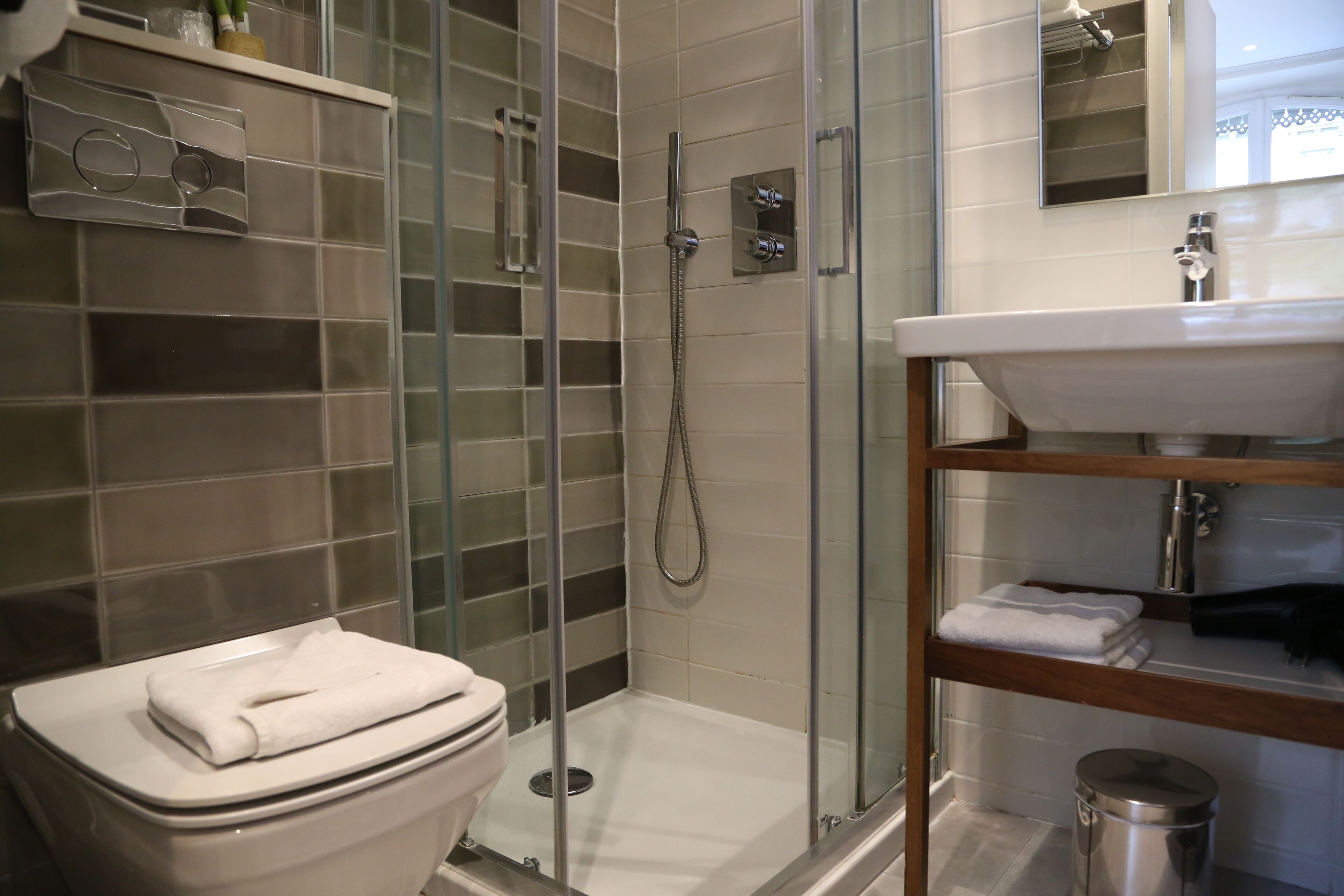 A modern bathroom with a glass-enclosed shower, a white toilet, and a sink with a wooden shelf.