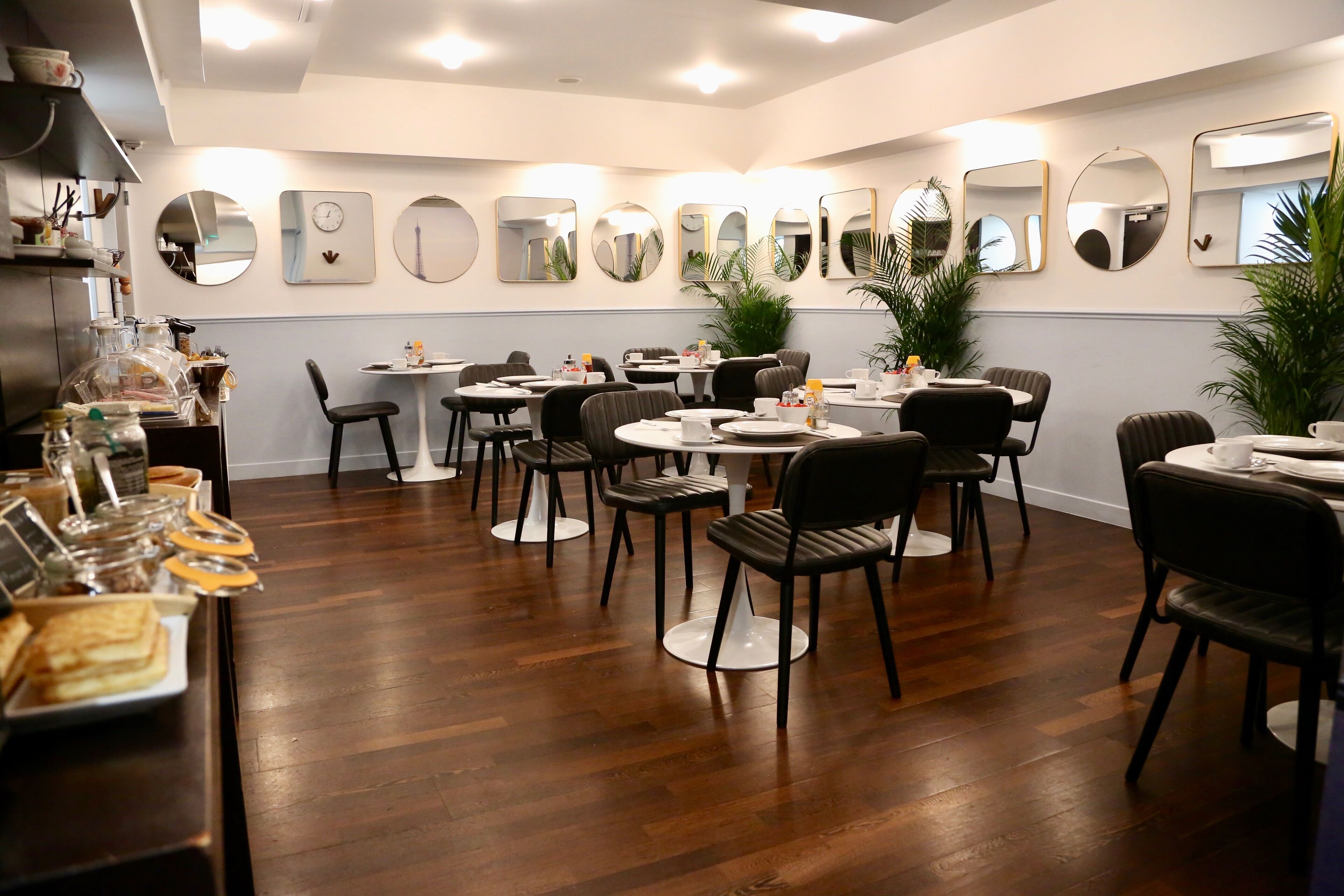 A dining area with round tables and chairs, a buffet with food items, and wall-mounted mirrors.