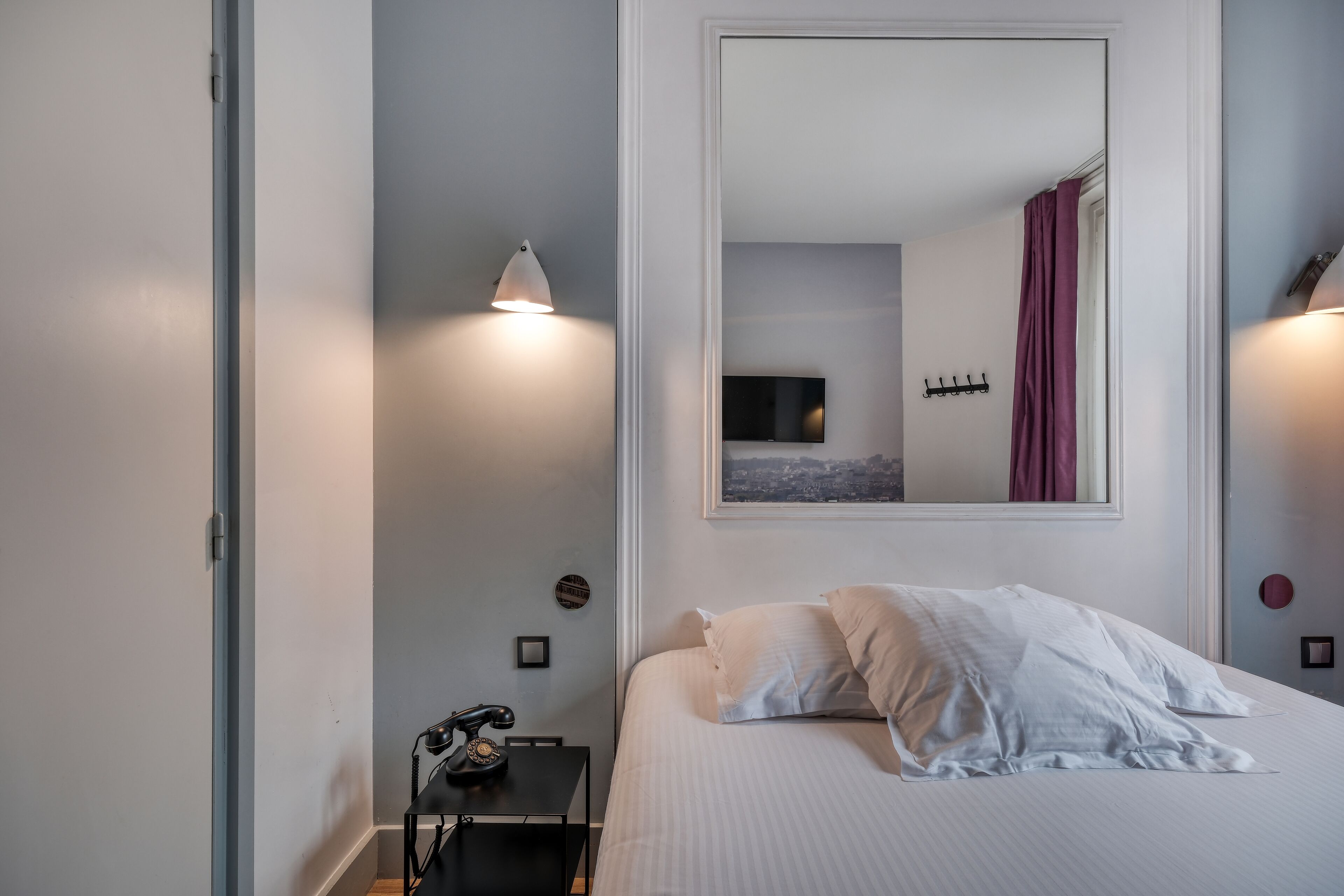 Une chambre d’hôtel comprenant un lit, un bureau avec un téléphone et deux lampes fixées au mur.