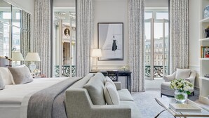 A hotel room with a large bed, a sofa, a desk with a lamp, and a view of the city through large windows. - InterContinental Paris le Grand by IHG (Paris)