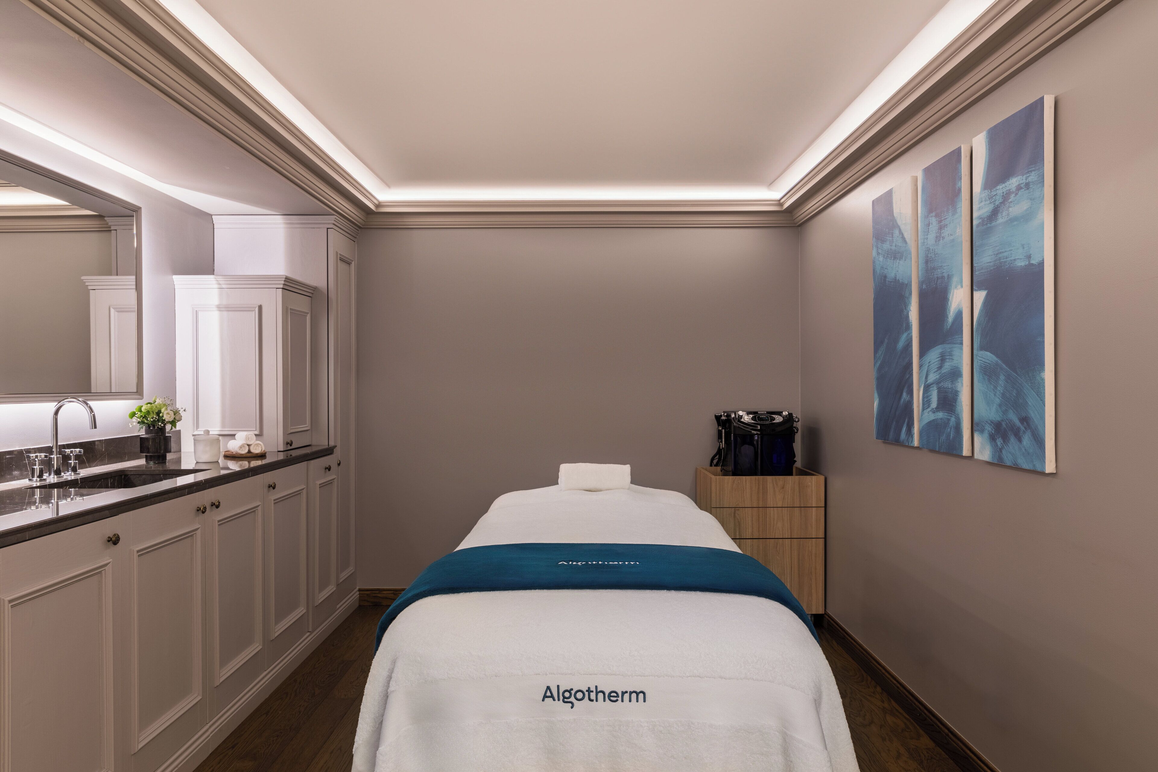 A spa room with a massage table, a sink, and a wooden cabinet.