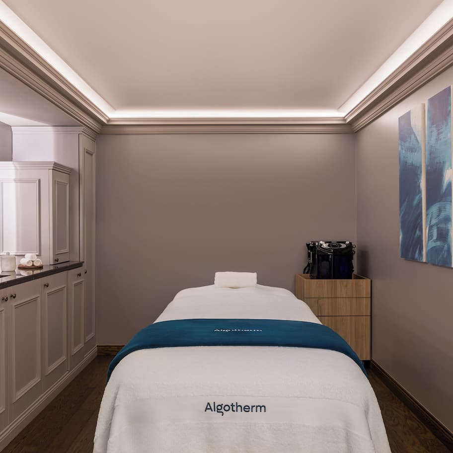 A spa room with a massage table, a sink, and a wooden cabinet.